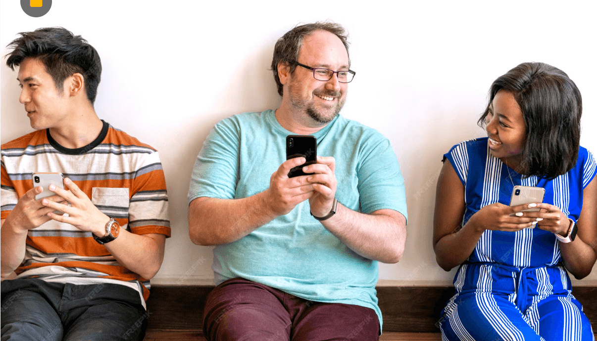 Three people sat against a wall, smiling and looking at phones